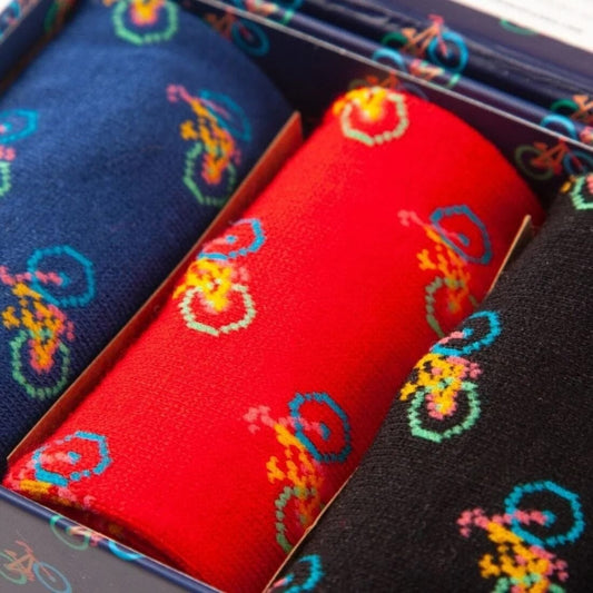A close up of 3 pairs of bamboo socks ina box. One pair is blue, 1 red and 1 black, all have a epeated multi-coloured bicycle motif.