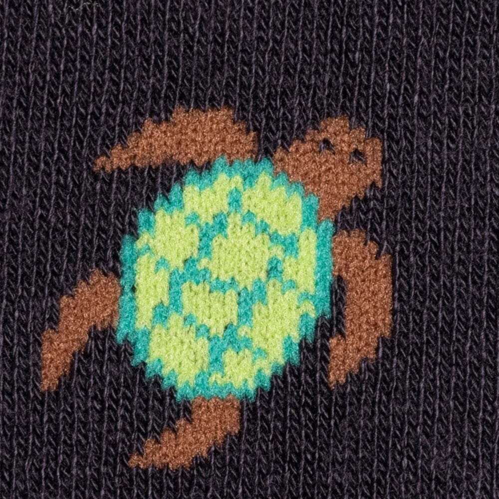 Close-up of a knitted textile featuring a turtle motif with a bright turquoise and lime green shell and brown flippers on a black background.