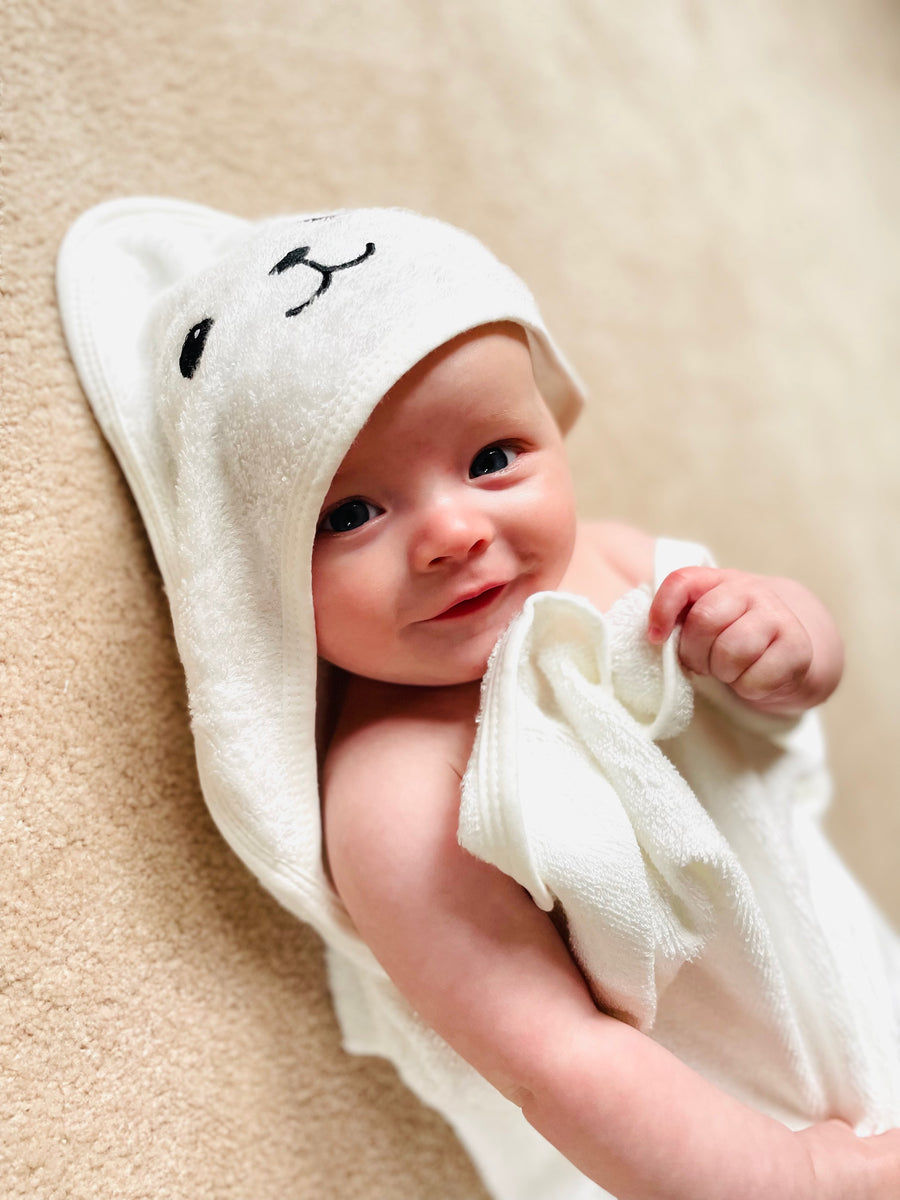 A baby wearing a bamboo hooded baby towel, with bear detail on the hood