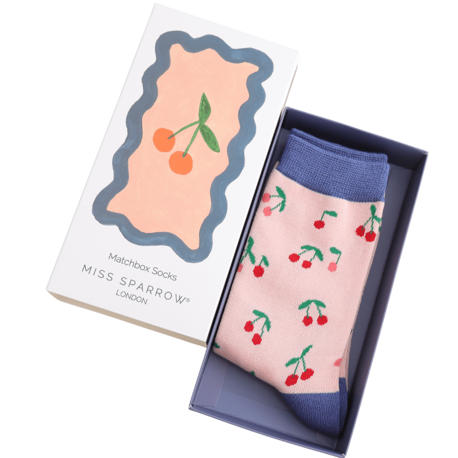 Open box, the lid is laid next to it and inside is a pair of pink and blue socks with cherry design.