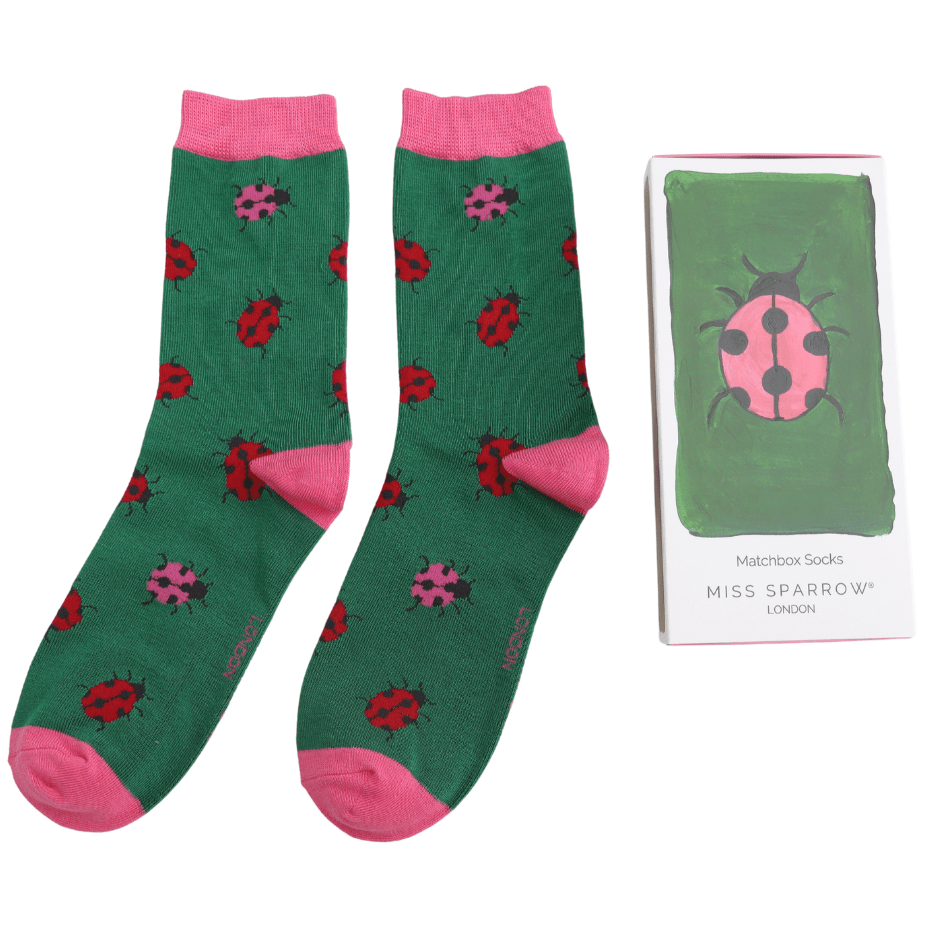 Green socks with pink accents and ladybird pattern next to a packaging box on a white background
