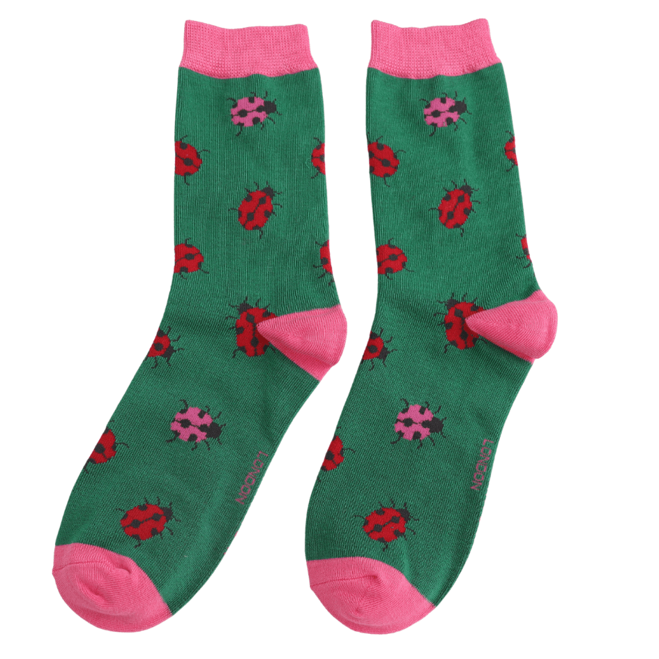 A pair of green crew socks with pink cuffs, heels, and toes, featuring a pattern of red and pink ladybirds, shown on a plain white background.