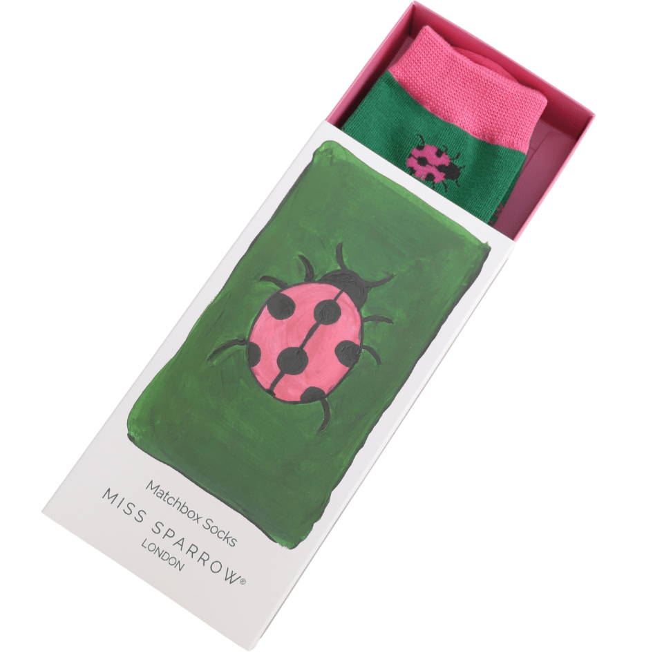 Matchbox style box, half slid opwn, revealing the top of a pai of green bamboo socks with pink cuff and ladybird design