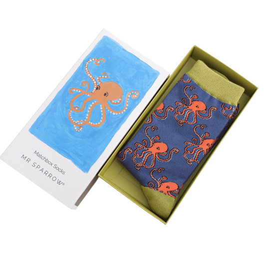 An open box containing  single pair of blue oskcs with green cuffs and toes and with an orange october design.  The lid of the box is placed next to it, also with an orange octobus design on a blue background, and the work Matchbox socks, Mr Sparrow below