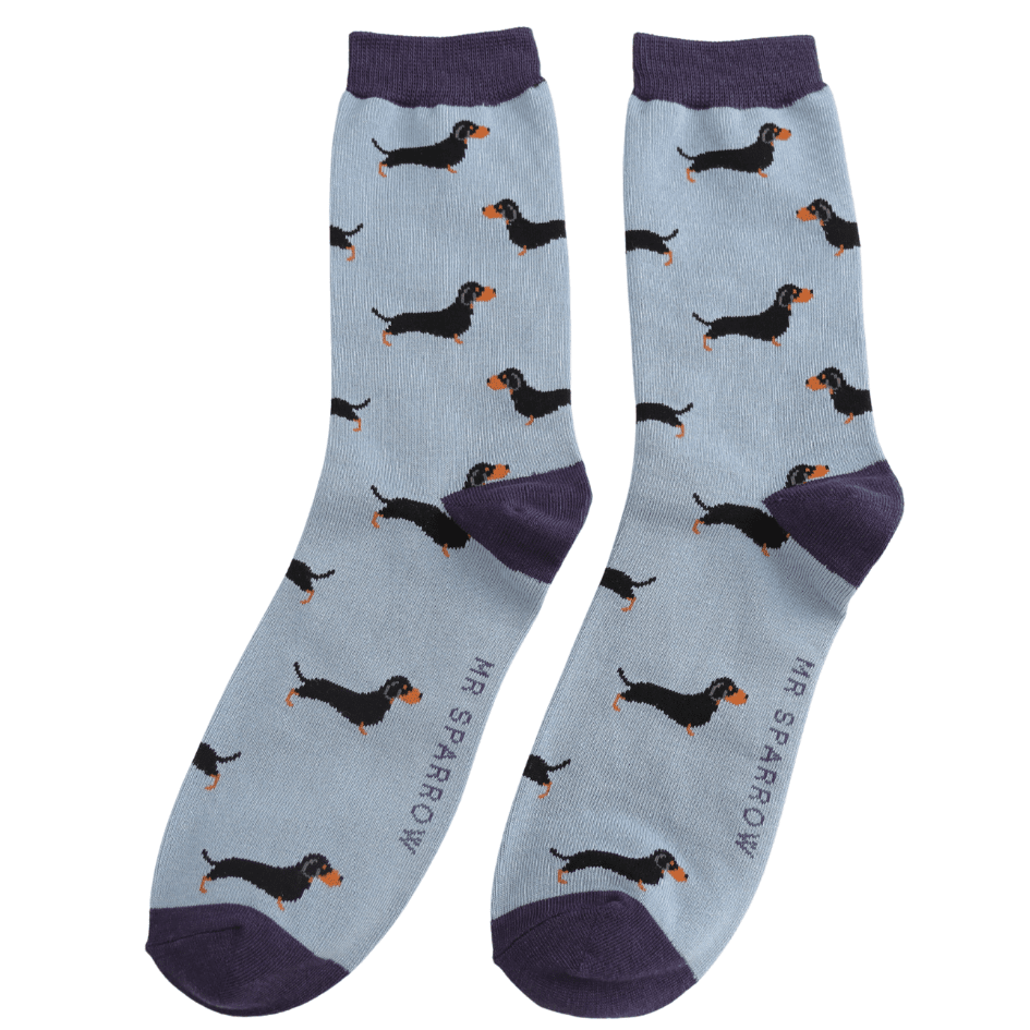 A pair of light blue crew socks with a repeating pattern of black dachshund dogs with orange accents, featuring darker cuffs, heels, and toes. The brand name 'MR SPARROW' is printed vertically on the sole of each sock.