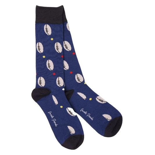 A pair of navy blue crew socks with a repeating pattern of white rugby balls and small colorful dots, featuring black heels, toes, and cuffs.