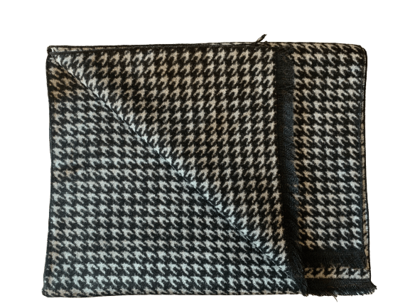 A folded houndstooth scarf in black and white, featuring a fringed edge and a zippered closure, shown against a plain white background.
