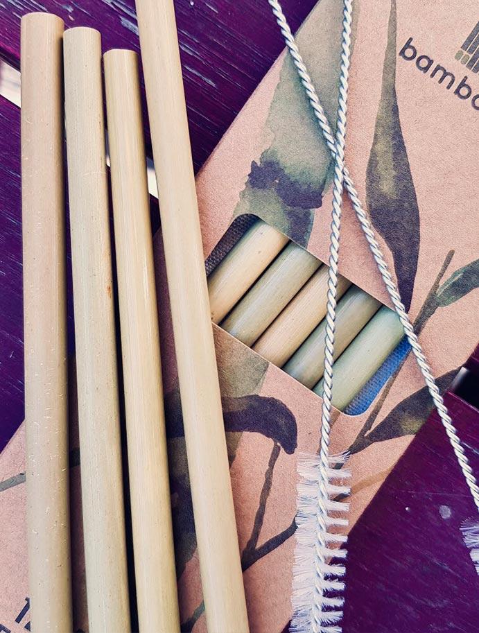 4 bamboo straws and 2 cleaning brushes arranged on top of the box they are packed in, with more straws still inside