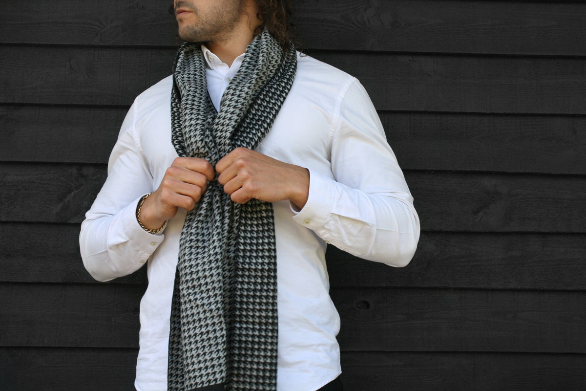 A man wearing a crisp white shirt with a black and white scarf with houndtoooth pattern draped around his neck 